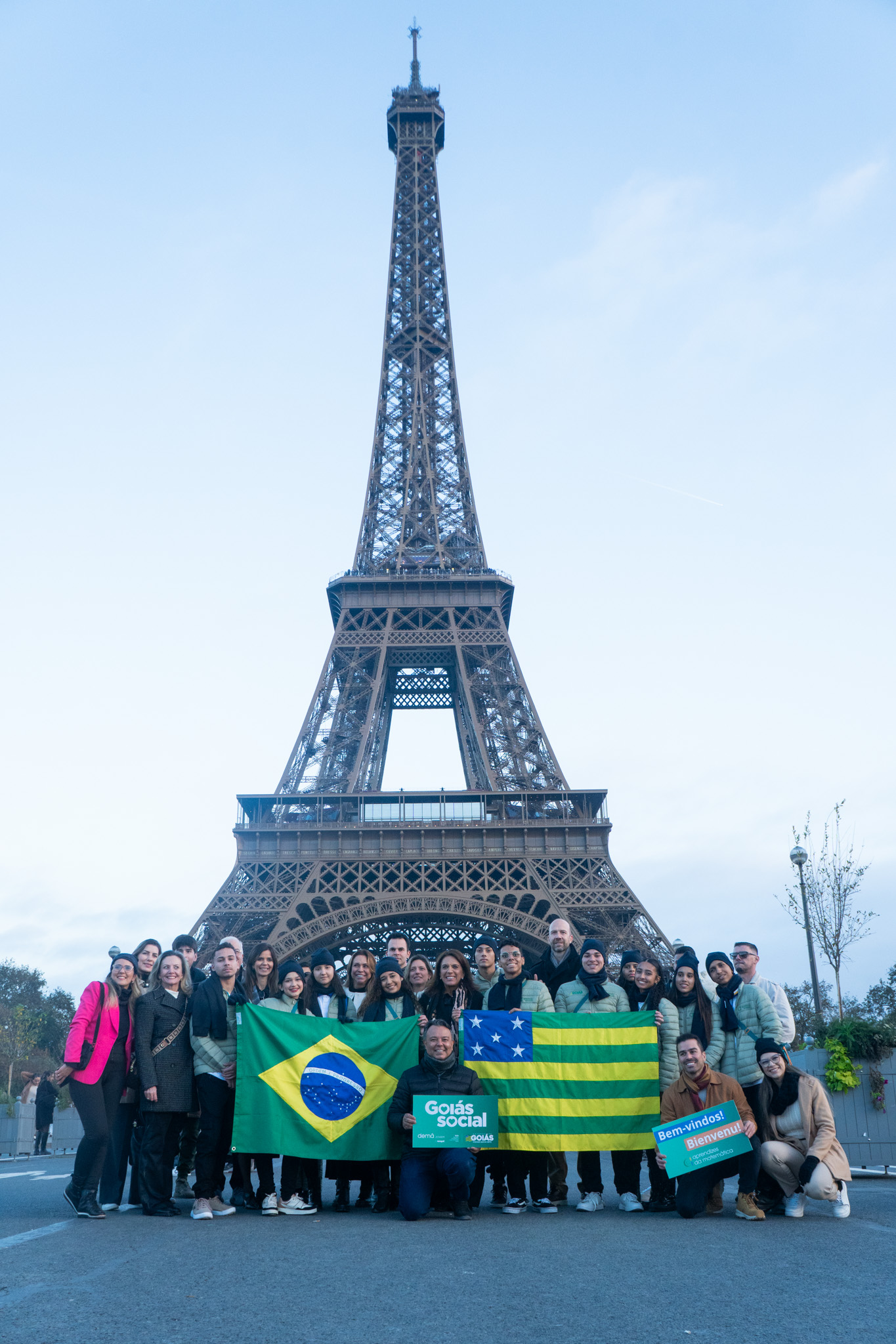 Grupo de jovens aprendizes de Goiás posa em frente à Torre Eiffel, em Paris, segurando bandeiras do Brasil e de Goiás, durante o intercâmbio internacional promovido pelo Programa Aprendiz do Futuro.