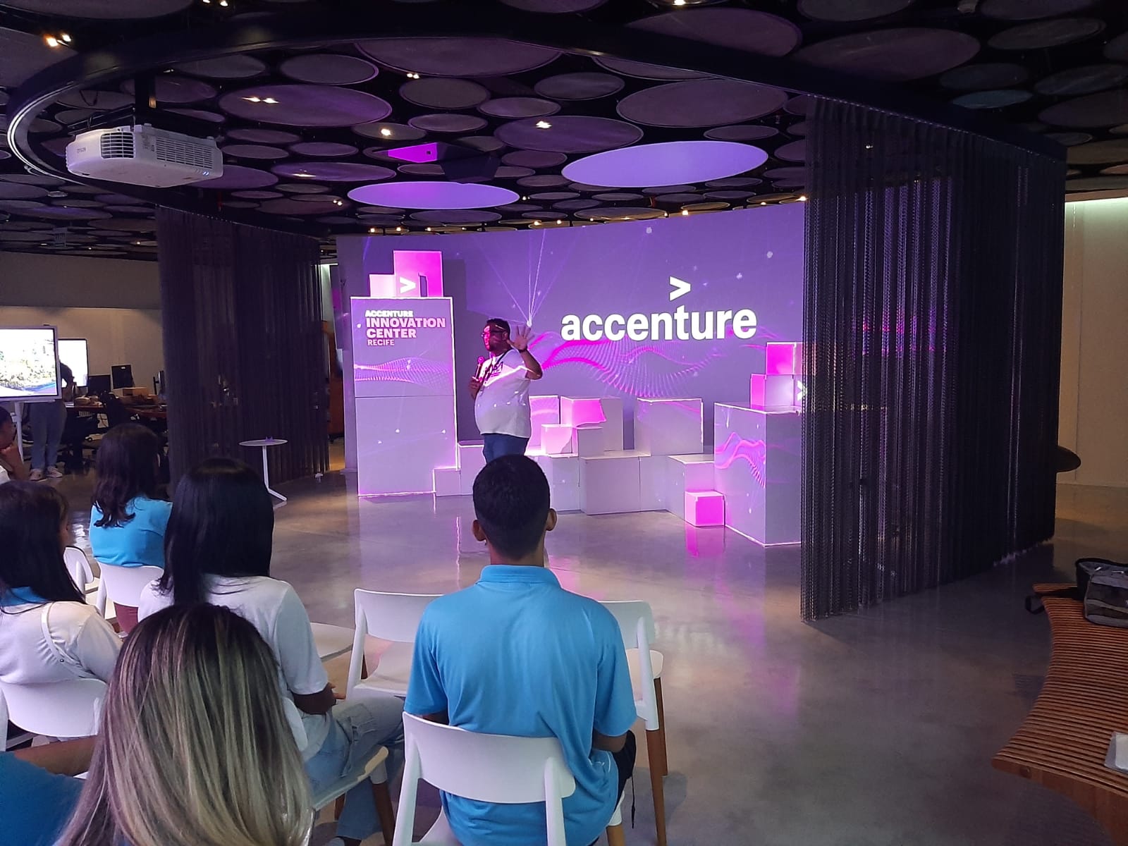  Instrutora conduz jovens aprendizes em uma conversa no Innovation Center da Accenture em Recife. Os participantes, atentos e entusiasmados, vivenciam a inovação e têm a oportunidade de explorar as possibilidades de carreira na área de tecnologia.