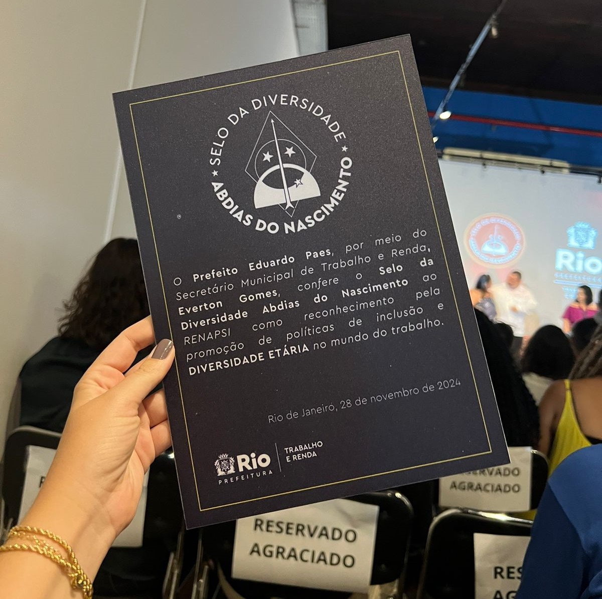 Placa de premiação do Selo da Diversidade Abdias do Nascimento, entregue à Renapsi pela Prefeitura do Rio de Janeiro. A placa destaca o reconhecimento à promoção de políticas inclusivas e de diversidade etária no mundo do trabalho. A imagem foi registrada durante a cerimônia de entrega, com o ambiente do evento ao fundo.